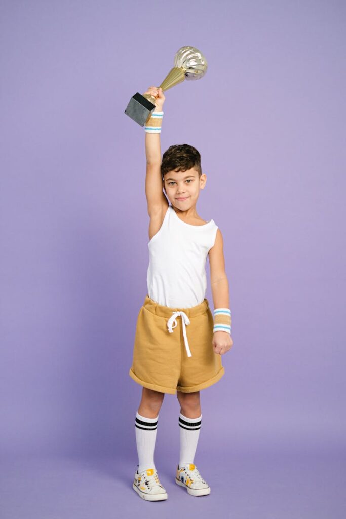 Confident young boy wearing casual attire holding a trophy triumphantly indoors.