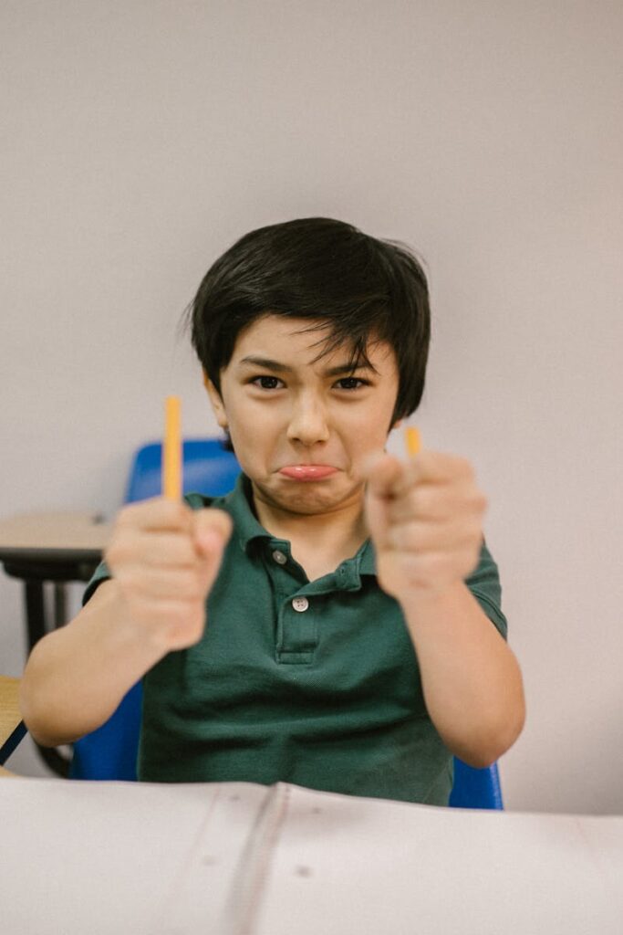 A young boy in a classroom showing frustration, holding broken pencils.